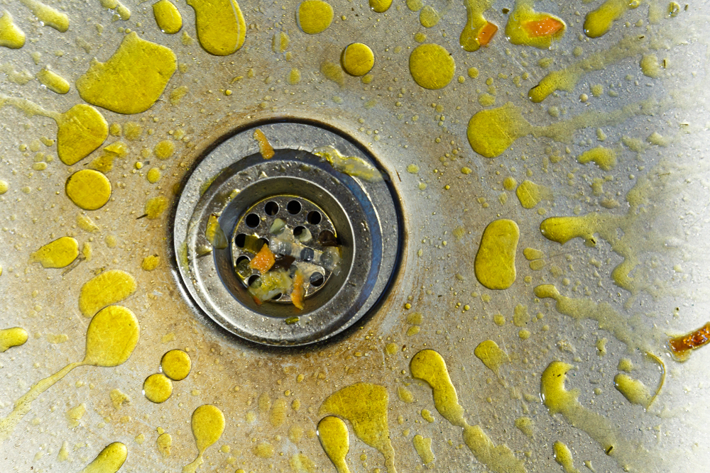 Fatty yellow liquid splotches around the drain of a metal kitchen sink.