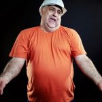 Man in white hardhat and orange shirt making exasperated gesture