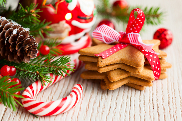 Holiday decorations, including pine, pinecone, berries, a Santa figurine, a candy cane, and several star-shaped cookies tied in a bow