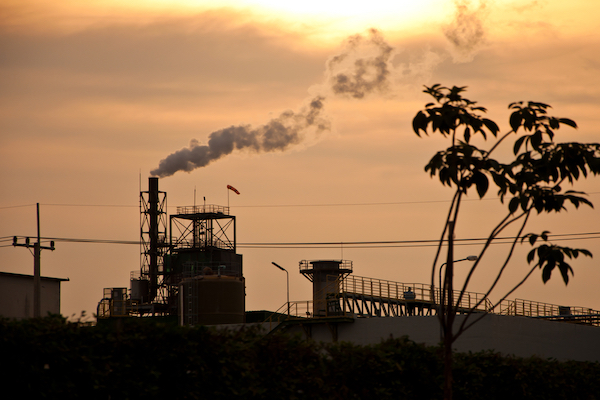 Factory in California's chimney giving off white smoke against orange sunset 