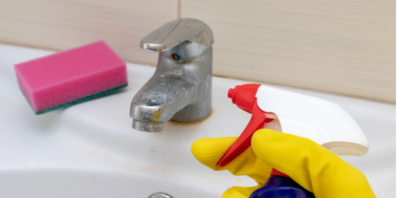 Spraying a cleaning solution onto a bathroom sink’s faucet