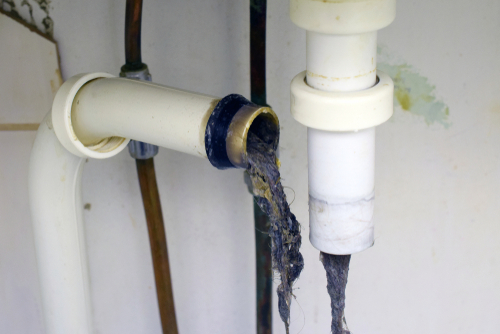 Beneath a bathroom sink, the P trap is removed and gunk sticks out from exposed pipes.