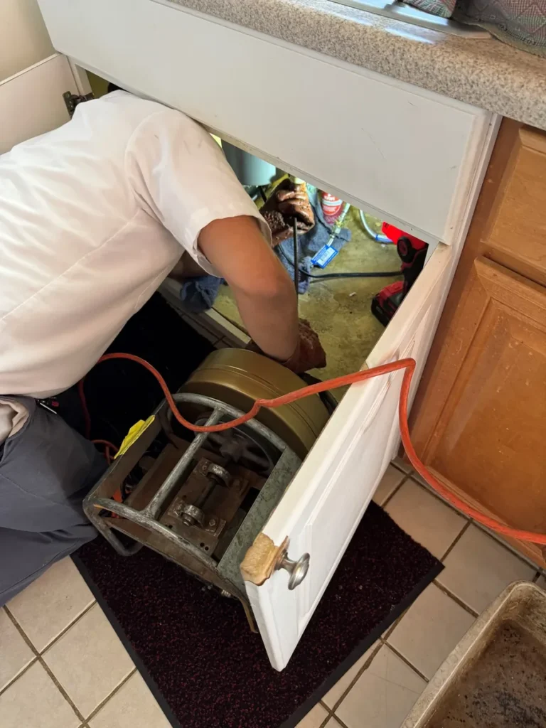 Plumber using drain-cabling equipment beneath a kitchen sink
