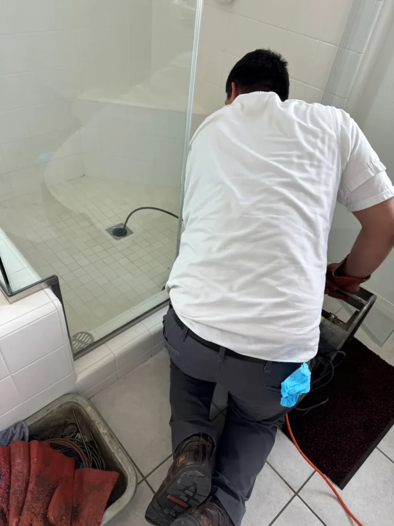Plumber clearing a shower drain with drain-cabling equipment